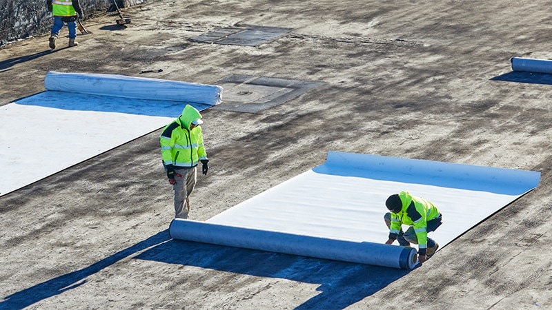 Contractors installing EverGuard® Fleece-Back single-ply membrane on a flat commercial rooftop.