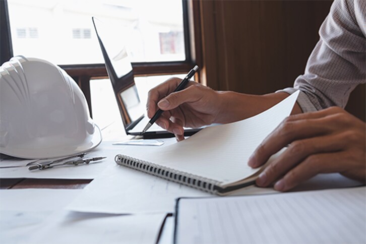 Person with notebook and pen, filling out application next to construction helmet.