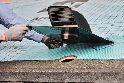 A contractor inserting the vent’s neck into a circular opening in the roof deck