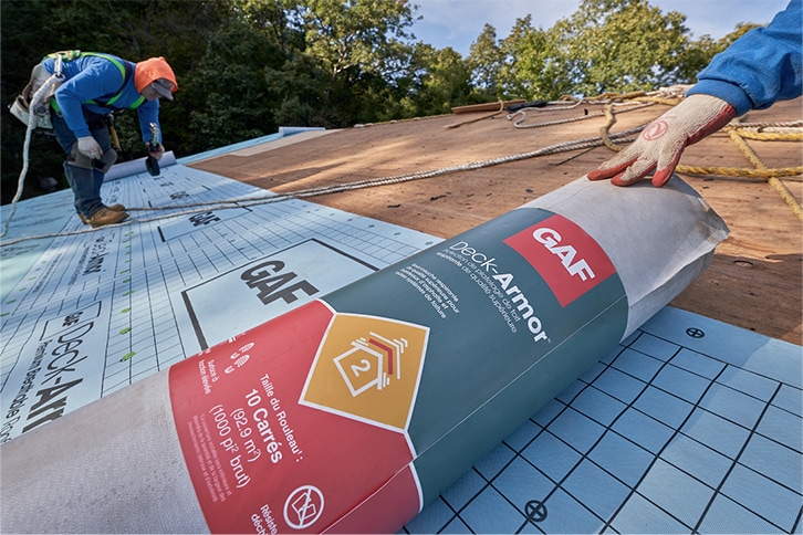 Contractors installing GAF synthetic roofing underlayment on a roof.